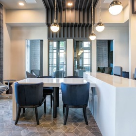 Clubroom kitchen and bar at Prime with a white island countertop, black chairs, stainless steel appliances, and large windows allowing for natural light