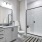 A modern bathroom featuring a walk-in shower with glass doors, a white vanity with a gray countertop, and a large mirror above the sink