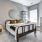 A modern bedroom featuring a wooden bed with white and green bedding, decorative yellow pillows, a circular mirror on the wall, a gray dresser, and natural light coming in