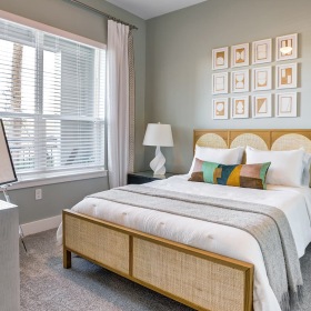 A neatly arranged bedroom at Prime with a beige upholstered bed, white bedding, decorative pillows, and two white table lamps on matching nightstands.